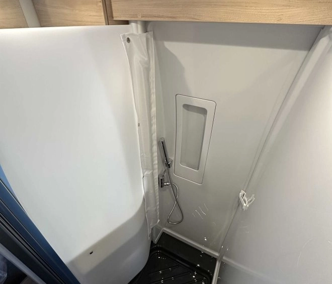 Douche compacte avec parois blanches et sol noir dans un camping-car moderne.