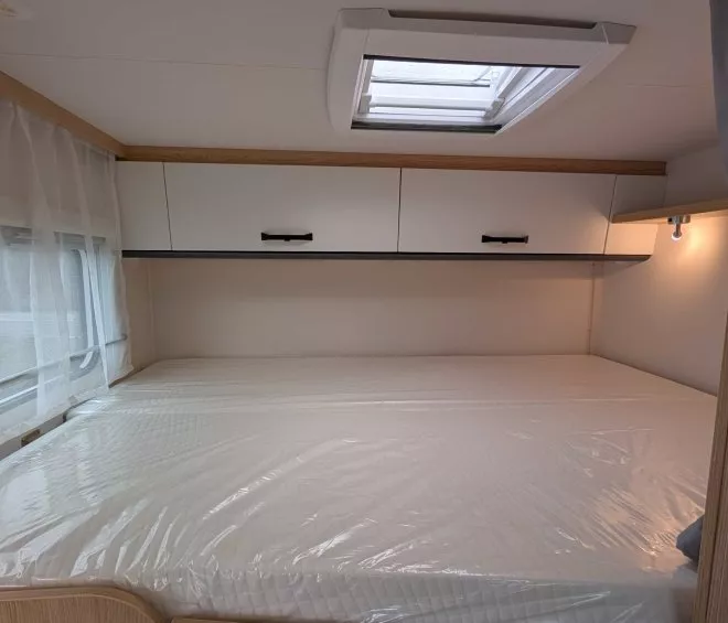 Intérieur d'une caravane avec lit double, placards et fenêtre avec rideau.
