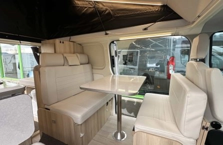 Intérieur d'un van aménagé avec sièges et table en bois clair, éclairage LED