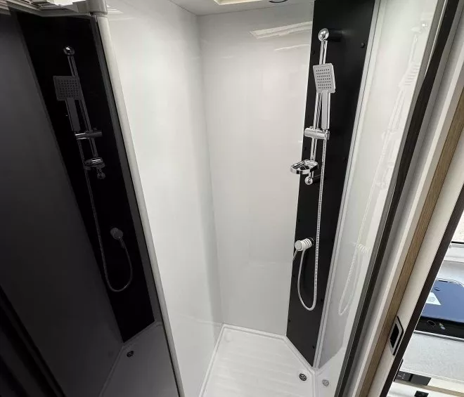 Douche moderne avec parois blanches et pommeau de douche chromé dans un camping-car.
