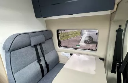 Intérieur d'un camping-car avec banquette et table pliante, vue sur fenêtre latérale.