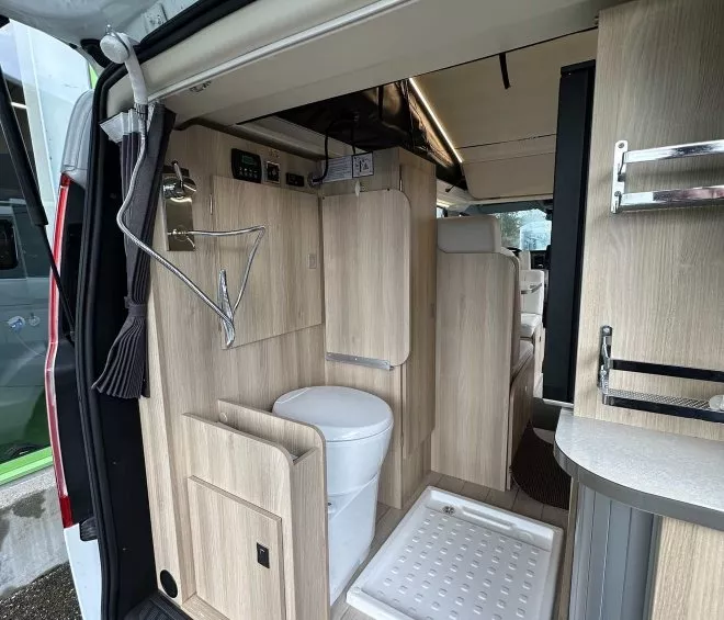 Intérieur d'un van aménagé avec douche et toilettes intégrées, mobilier en bois clair.