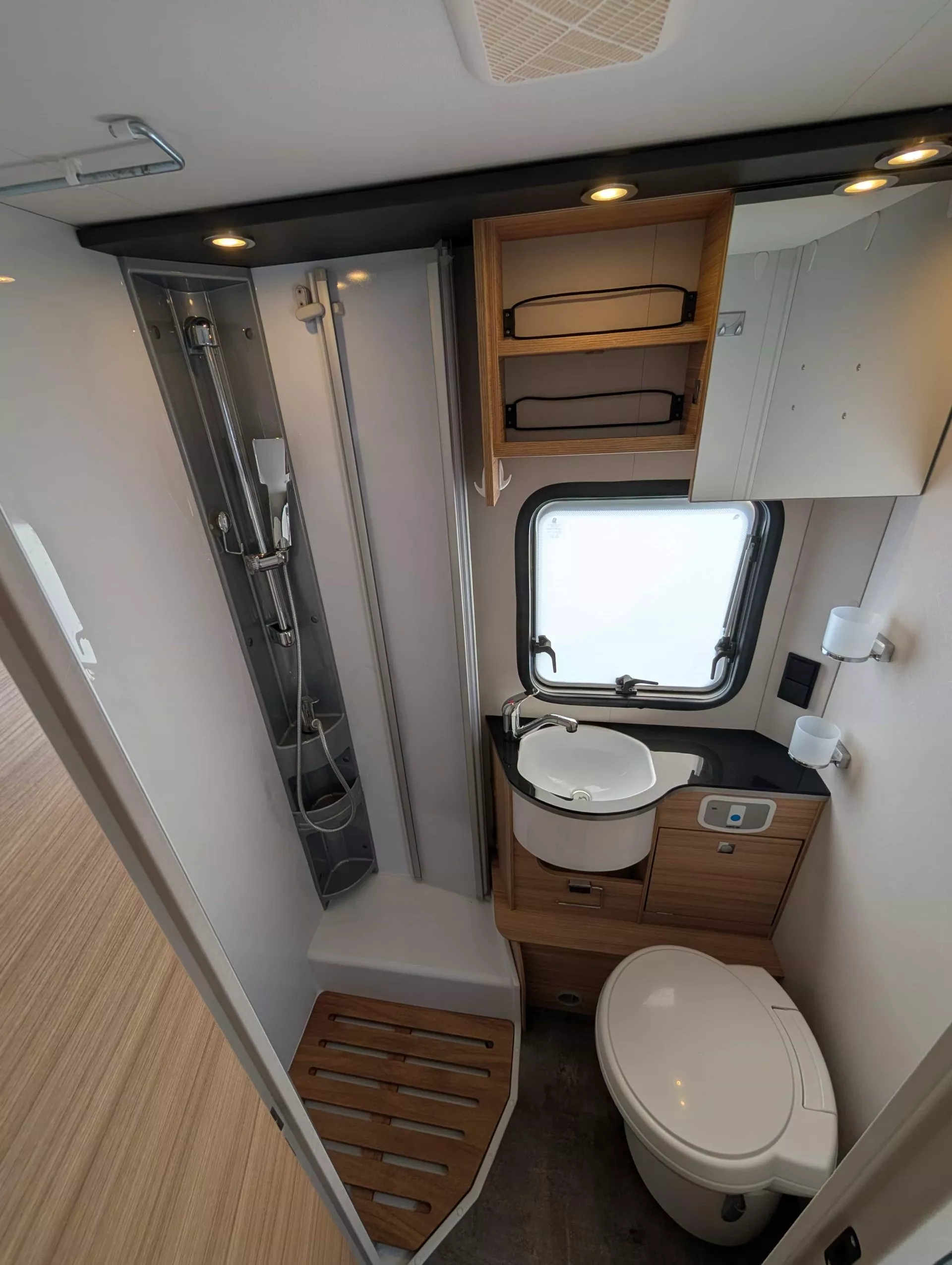 Salle de bain compacte avec douche, lavabo et toilettes dans un camping-car moderne.