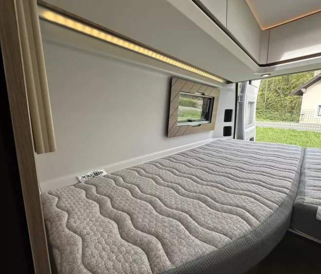 Intérieur d'un van aménagé avec lit double et fenêtre ouverte sur jardin