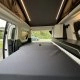Intérieur d'un van aménagé avec lit pliable et rangements, vue sur l'extérieur