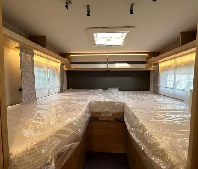 Intérieur d'une caravane avec lits jumeaux sous un puits de lumière.