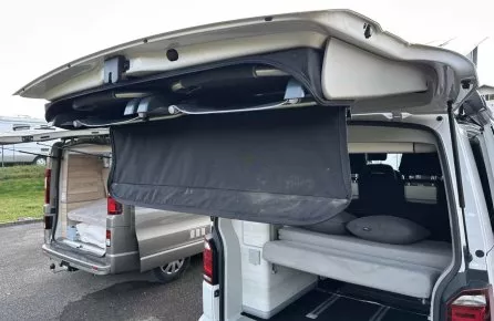 Vans aménagés avec lits rabattables et hayons ouverts sur un parking.