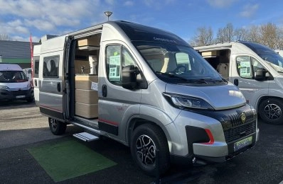 Camping-car gris avec porte latérale ouverte sur un parking