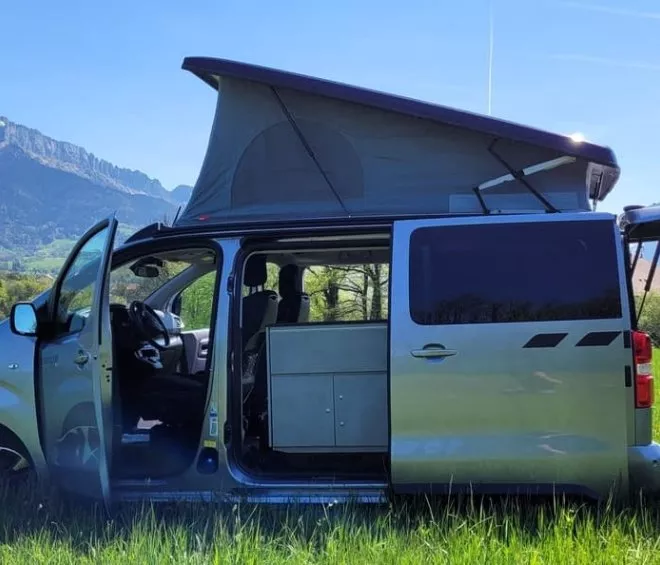 Van aménagé avec toit relevable dans un champ, montagnes en arrière-plan