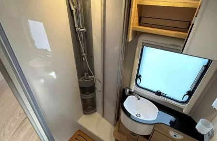 Salle de bain compacte dans un camping-car avec douche, lavabo et toilettes.