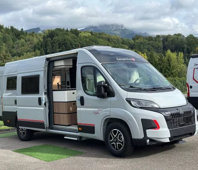 Camping-car blanc stationné devant une forêt verdoyante