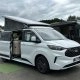 Van aménagé Ford blanc avec toit relevable sur un parking