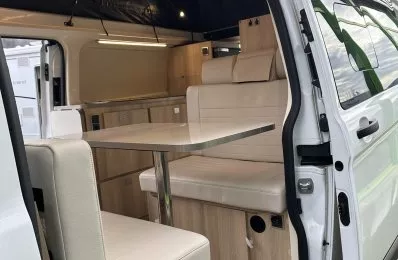 Intérieur d'un van aménagé avec table et banquettes en bois clair.