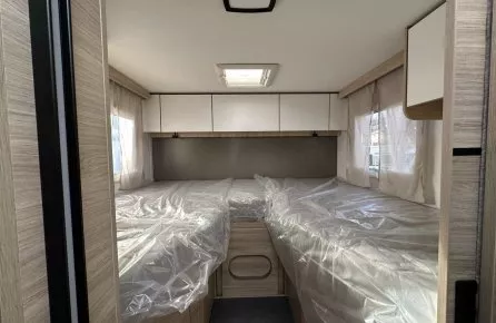 Intérieur d'une caravane avec lits jumeaux sous plastique, fenêtres latérales et placards.