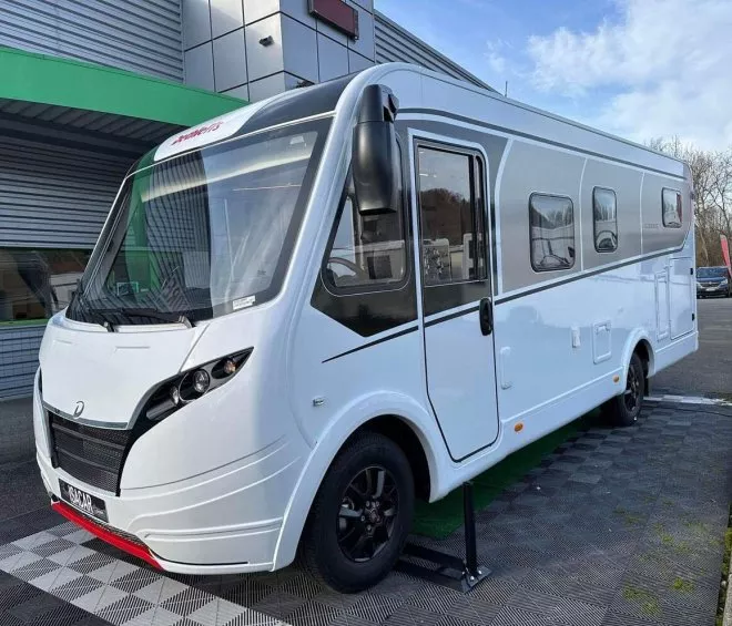 Camping-car blanc stationné devant un bâtiment moderne
