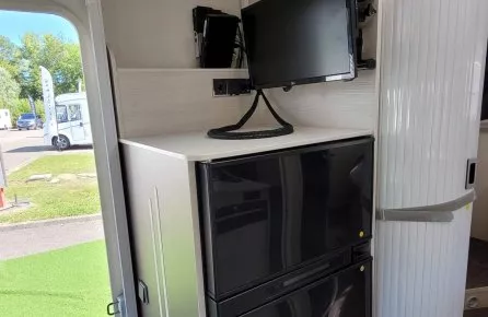 Intérieur d'un camping-car avec réfrigérateur, écran et panneau de contrôle.