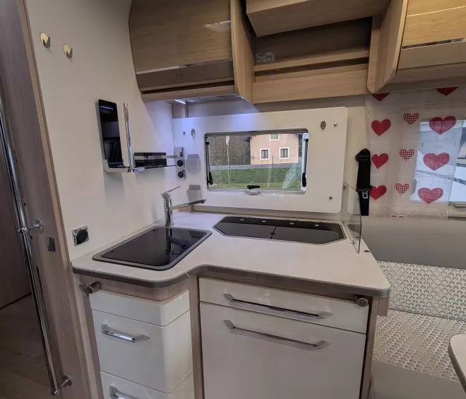 Cuisine compacte de camping-car avec évier, plaques de cuisson et rangements en bois clair.