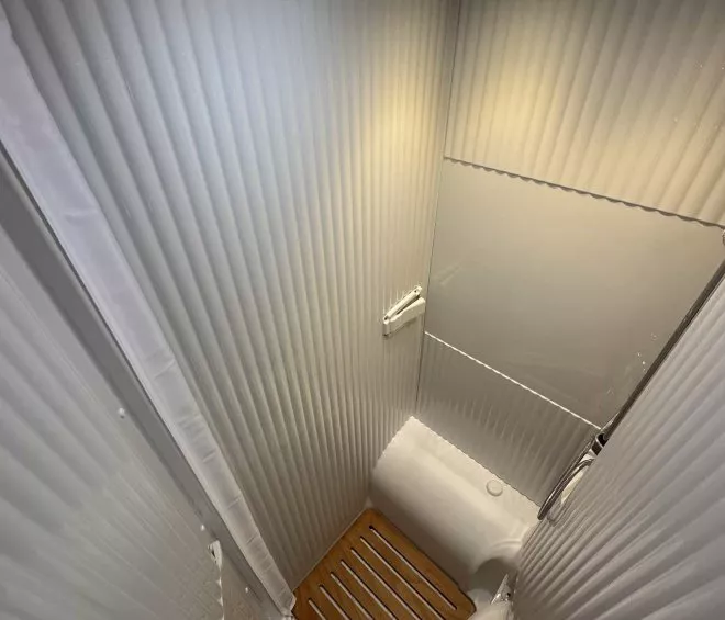 Douche compacte avec parois blanches et sol en bois, éclairage intégré, vue depuis le haut.