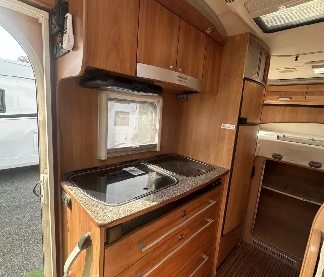 Cuisine intégrée en bois dans un camping-car avec plaques de cuisson et rangements.
