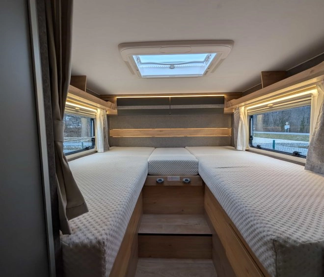 Intérieur d'un camping-car avec deux lits simples et fenêtres latérales.