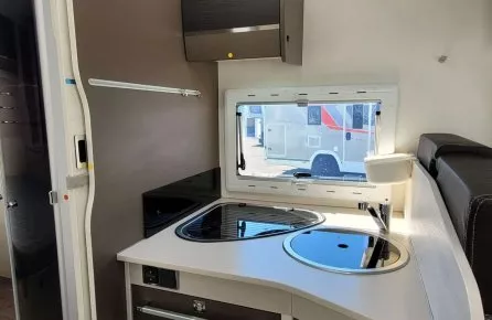 Cuisine compacte de camping-car avec évier, plaque de cuisson et fenêtre.