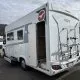 Camping-car Pilote stationné sur un parking avec porte ouverte et porte-vélos à l'arrière.