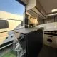 Intérieur d'un camping-car moderne avec cuisine et lit, vue sur l'extérieur ensoleillé