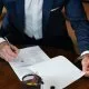 Personne en costume signant un document sur une table en bois