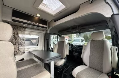 Intérieur d'un camping-car moderne avec sièges et table, vue sur l'extérieur.