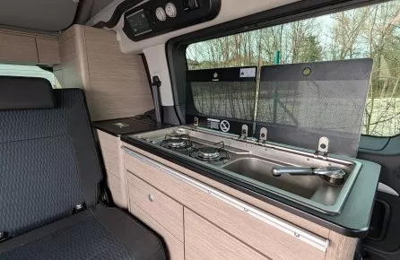 Intérieur d'un van aménagé avec cuisine intégrée et sièges en tissu noir.
