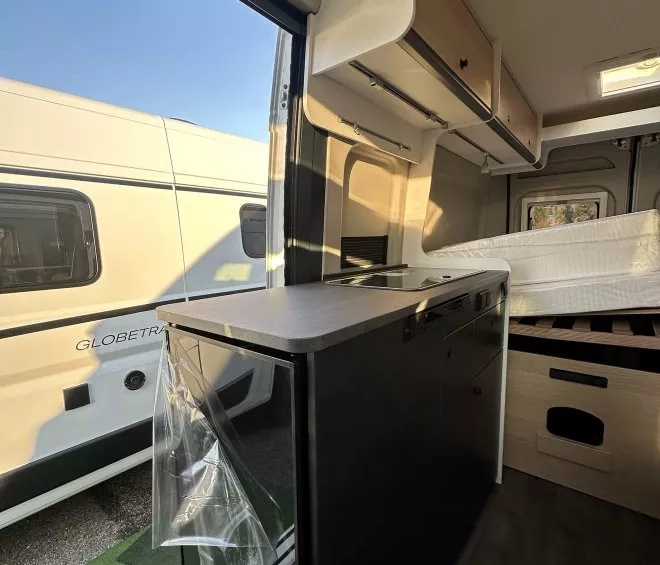Intérieur d'un camping-car moderne avec cuisine et lit, vue sur l'extérieur ensoleillé