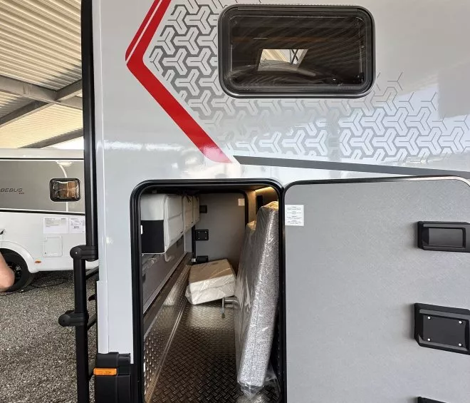 Compartiment de rangement ouvert d'une caravane sous abri, avec matelas emballé à l'intérieur.