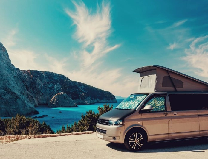 Van aménagé stationné devant une falaise et une mer turquoise sous un ciel bleu
