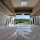 Intérieur d'un van aménagé avec vue sur la campagne verdoyante par la porte arrière ouverte.