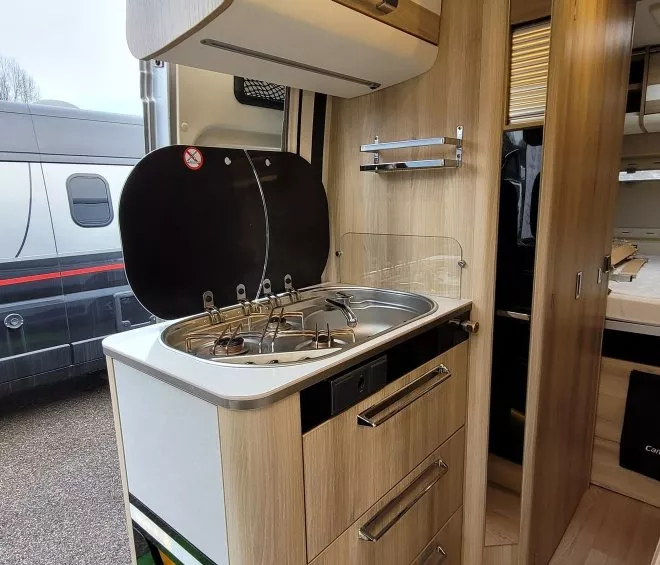 Cuisine compacte en bois dans un camping-car moderne avec plaques de cuisson et rangements.