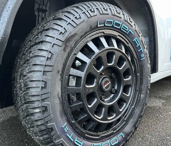 Pneu Loder AT monté sur une jante noire, véhicule stationné sur sol humide.