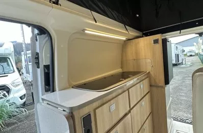 Intérieur d'un van aménagé avec cuisine en bois clair et éclairage LED.