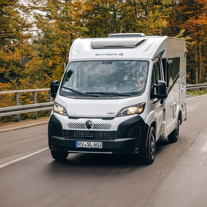 Camping-car Sunlight V60 roulant sur une route bordée d'arbres en automne.
