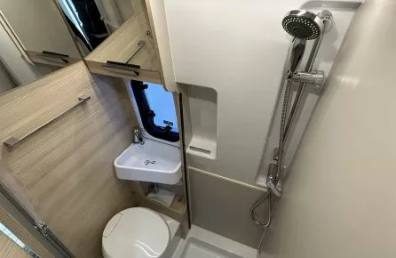 Salle de bain compacte avec douche, lavabo et toilettes dans un camping-car moderne.