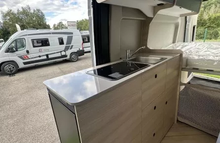 Intérieur d'un camping-car moderne avec cuisine équipée et lit, vue sur l'extérieur.