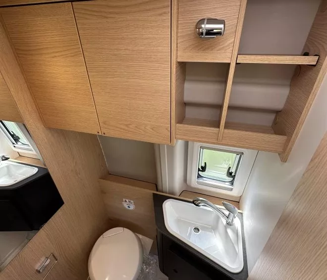 Salle de bain compacte en bois clair avec lavabo et toilettes dans un camping-car moderne.