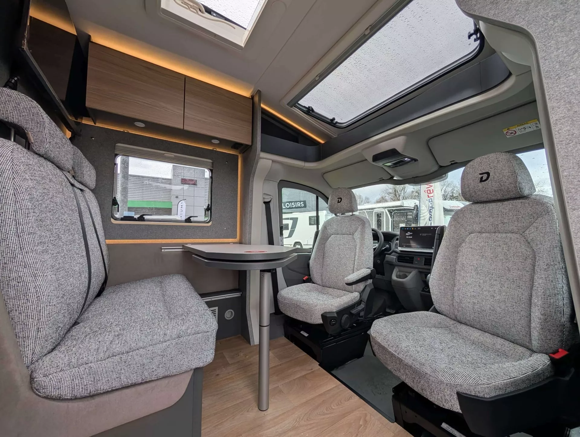 Intérieur d'un camping-car moderne avec sièges en tissu gris et table pliante.