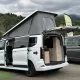 Van aménagé avec toit relevable et portes ouvertes, stationné en extérieur