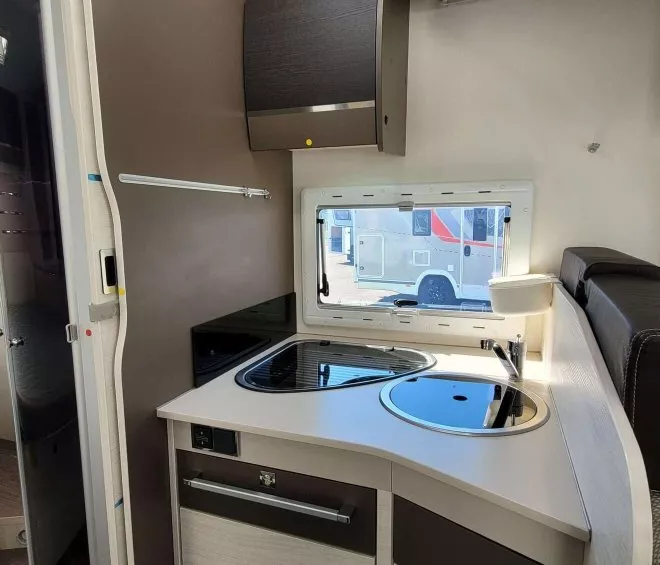 Cuisine compacte de camping-car avec évier, plaque de cuisson et fenêtre.