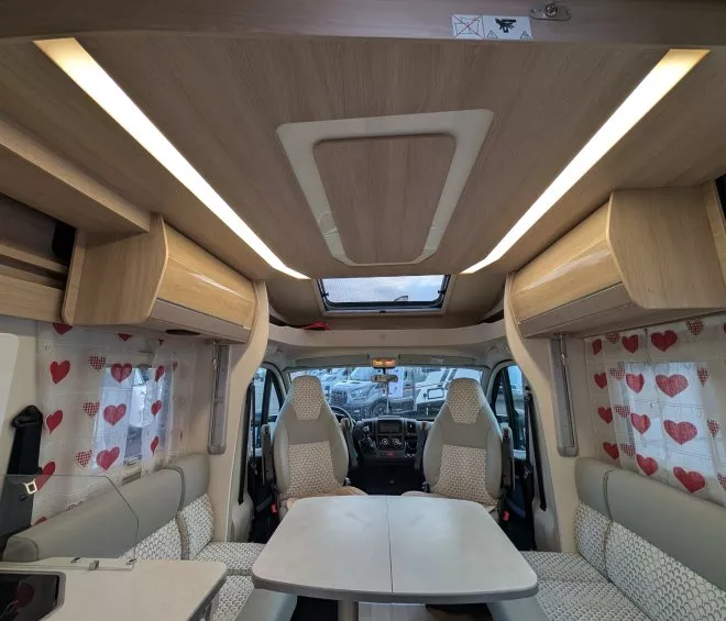 Intérieur d'un camping-car moderne avec sièges et table, rideaux à motifs de cœurs.