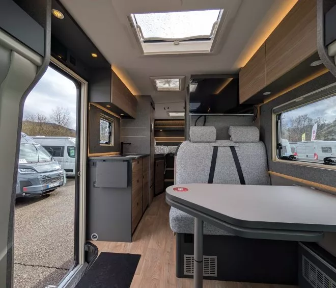 Intérieur d'un camping-car moderne avec table et sièges, vue sur l'extérieur.