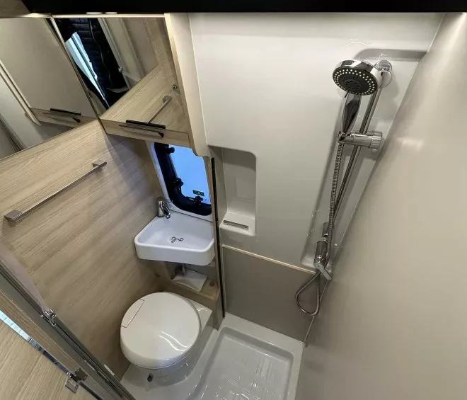 Salle de bain compacte avec douche, lavabo et toilettes dans un camping-car moderne.
