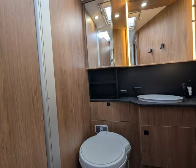 Salle de bain moderne en bois avec toilettes et lavabo dans un camping-car.