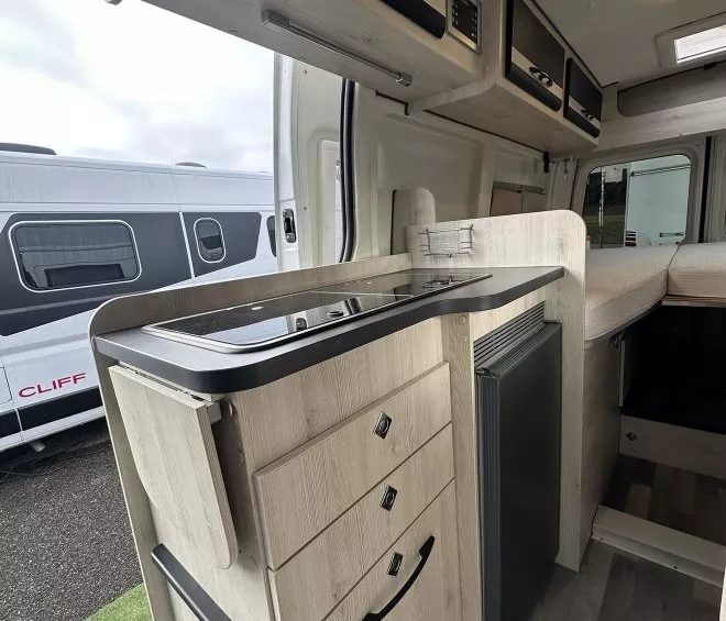 Intérieur d'un van aménagé avec cuisine intégrée et rangements en bois clair.