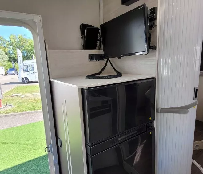 Intérieur d'un camping-car avec réfrigérateur, écran et panneau de contrôle.
